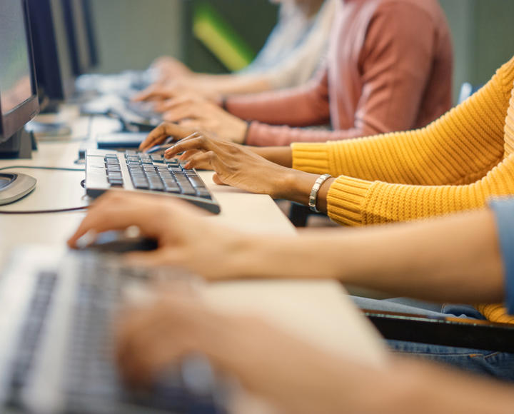 A row of people's hands, typing on a computer.