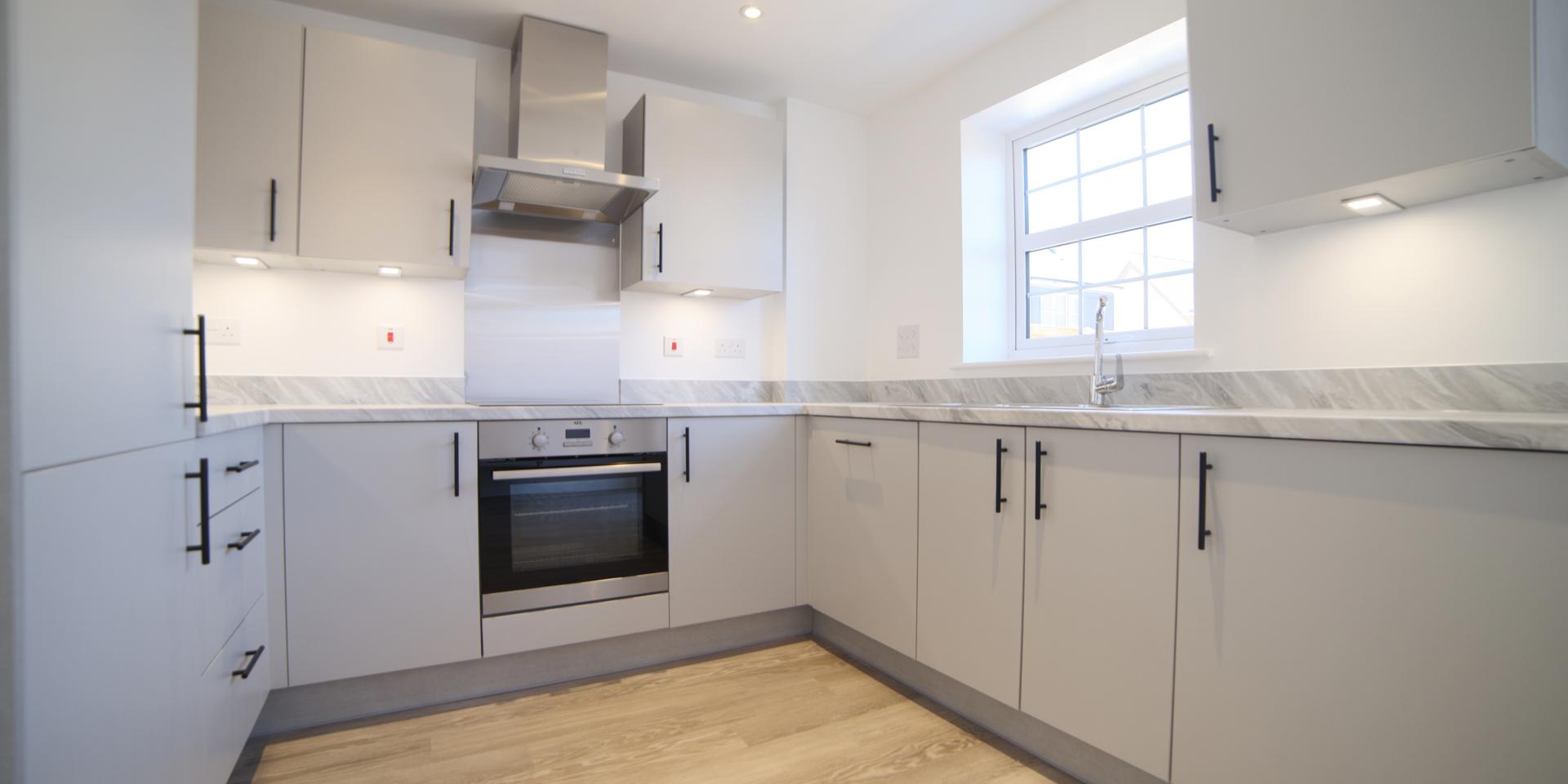 The kitchen has grey fitted cupboards with black handles and integrated appliances including a fridge freezer, dishwasher and washing machine