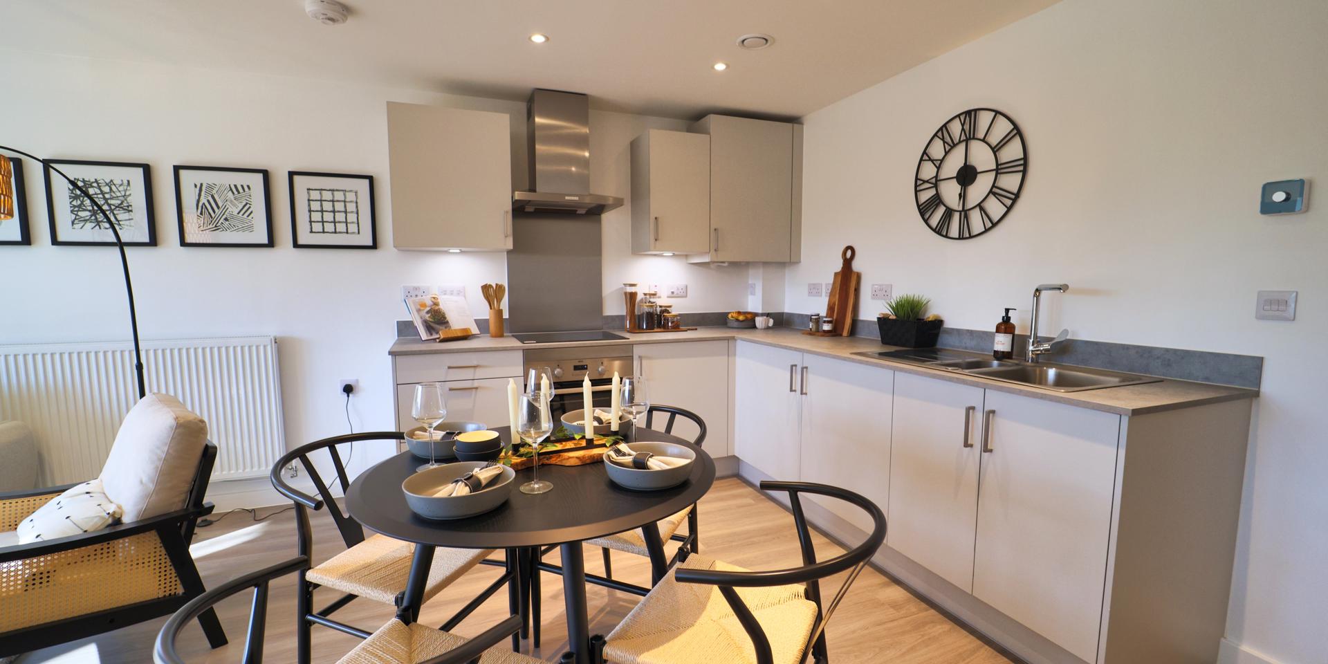 There is an l-shaped kitchen with grey units and worktop and a small round dining table and 4 chairs