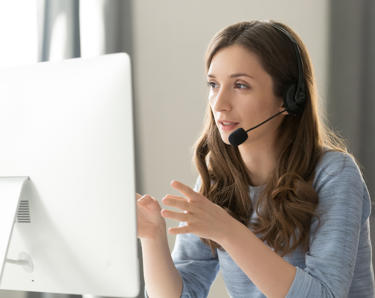 A woman on a computer, talking to someone on the phone.