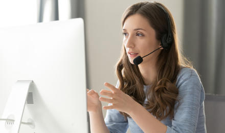 A woman on a computer, talking to someone on the phone.