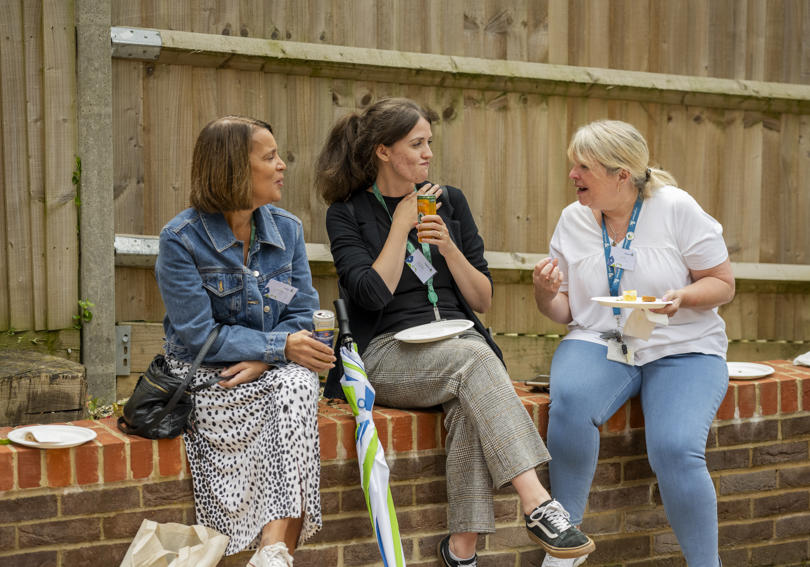 Hightown staff sitting on a wall chatting and eating cake at the Alexandra Road opening event
