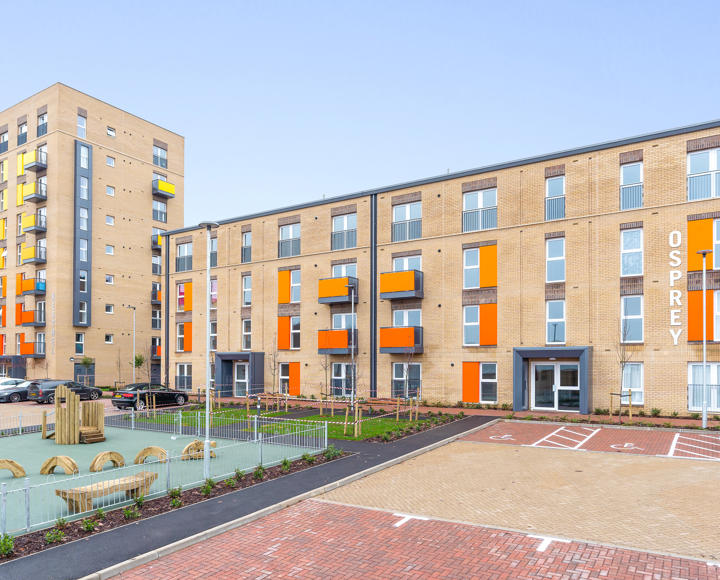 A long row of flats with orange and yellow balconies. In front of them there is a play park.