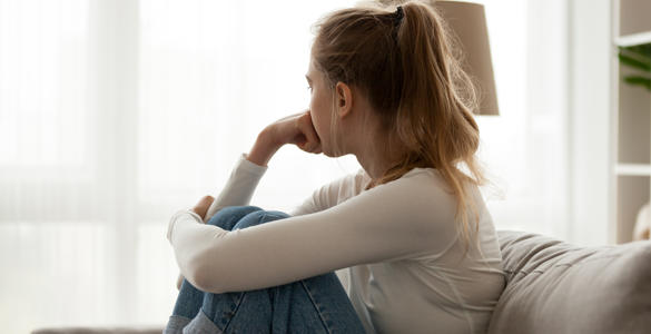A young woman, sitting on the sofa, with her head turned away from the camera.