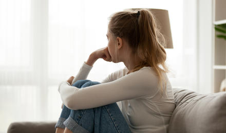 A young woman, sitting on the sofa, with her head turned away from the camera.