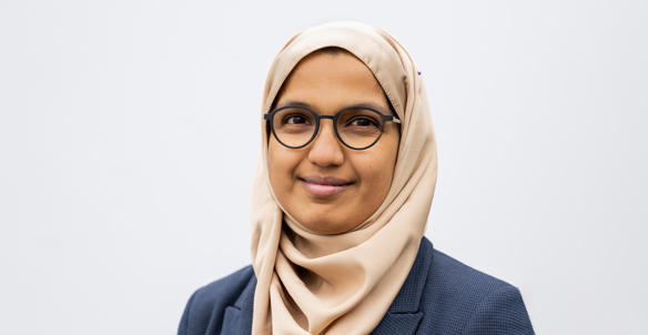 Headshot of a member of Hightown's Board, Zeena Farook. She is young and is wearing glasses and a blue checked blazer.