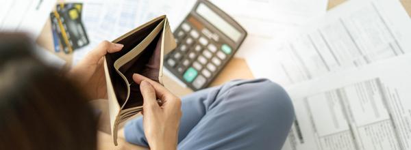 A person is looking inside an empty wallet and has a calculator and paperwork on the floor. They're trying to work out their finances to pay the rent. 