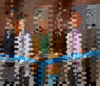 Debbie Jinks, Cllr Mione Goldspink and Andrew Royall. Cllr Goldspink is cutting a ribbon with gold scissors in front of a block of flats.