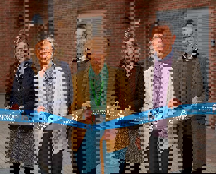 Debbie Jinks, Cllr Mione Goldspink and Andrew Royall. Cllr Goldspink is cutting a ribbon with gold scissors in front of a block of flats.