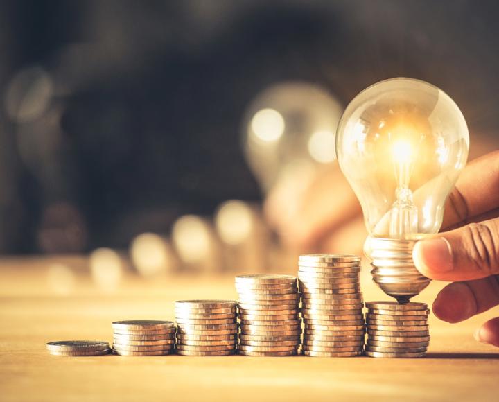 Coins piled on top of each with a hand holding a lightbulb above the coins
