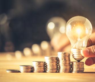 Coins piled on top of each with a hand holding a lightbulb above the coins