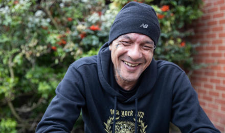 Man outside with black hoodie and hat on laughing