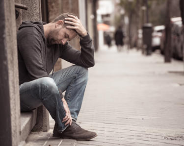 A man sat on a step on the pavement, holding his head in his hands.