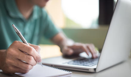 A man looking at his laptop and making notes 