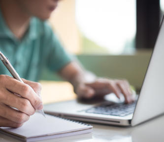 A man looking at his laptop and making notes 