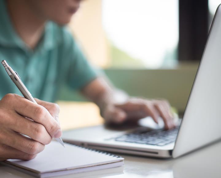 A man looking at his laptop and making notes 