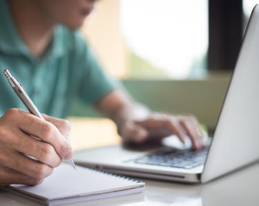 A man looking at his laptop and making notes 