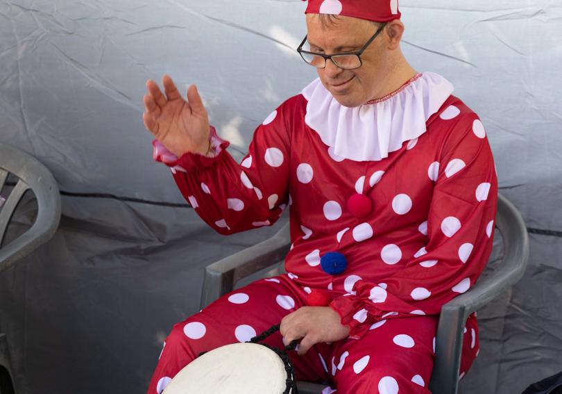 A service user in fancy dress smiles and plays the bongo drums