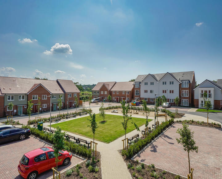 A square communal grass area surrounded by new build flats and houses. Taken on a sunny day. 