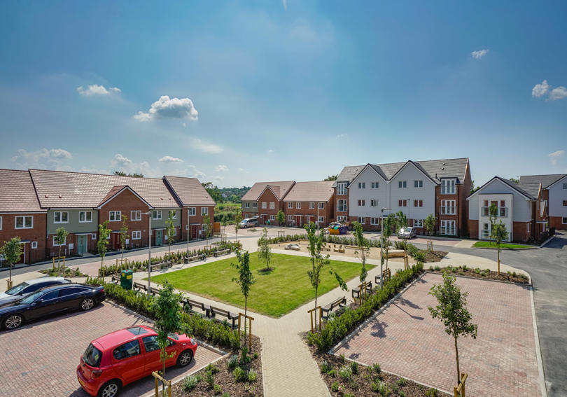 A square communal grass area surrounded by new build flats and houses. Taken on a sunny day. 