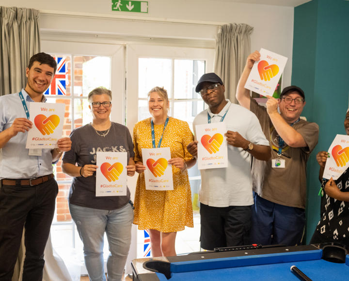 Staff standing and smiling holding #GladtoCare signs