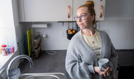 A woman standing in the kitchen, holding a cup of tea and staring out of the window