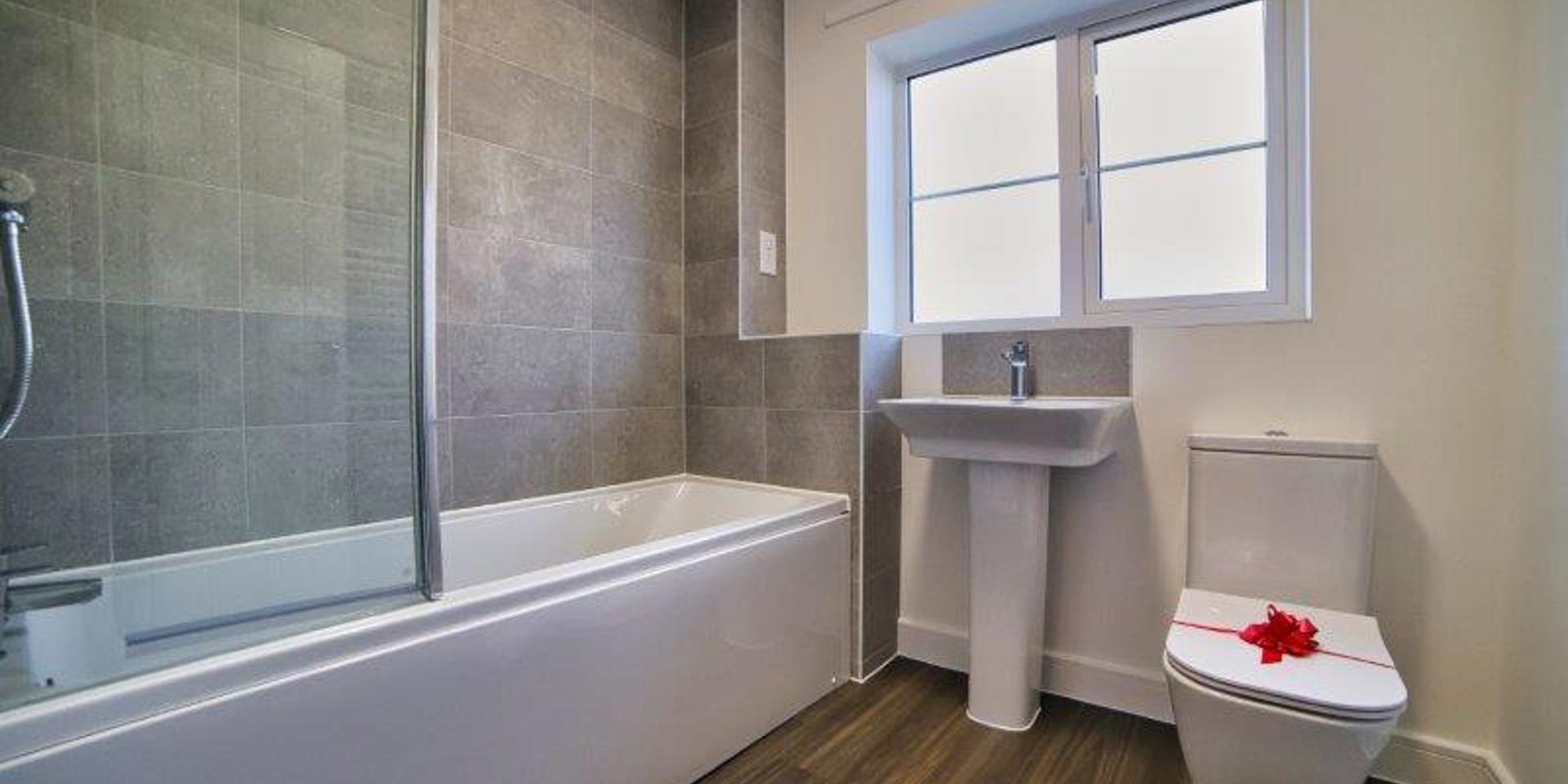 View of the bathroom including the bath with shower, toilet and wash hand basin