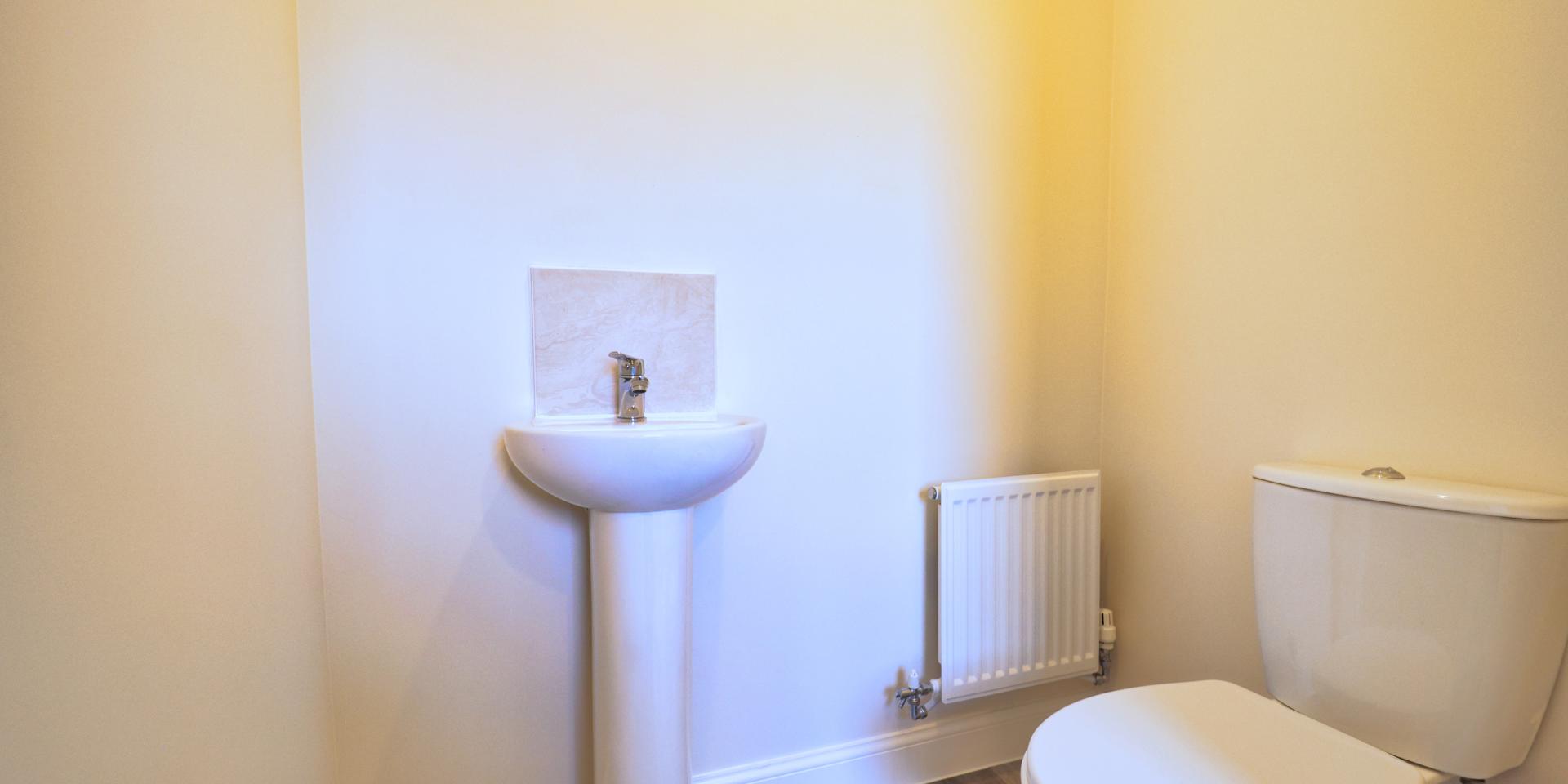 A white WC and wash hand basin. The cloakroom is located off the kitchen