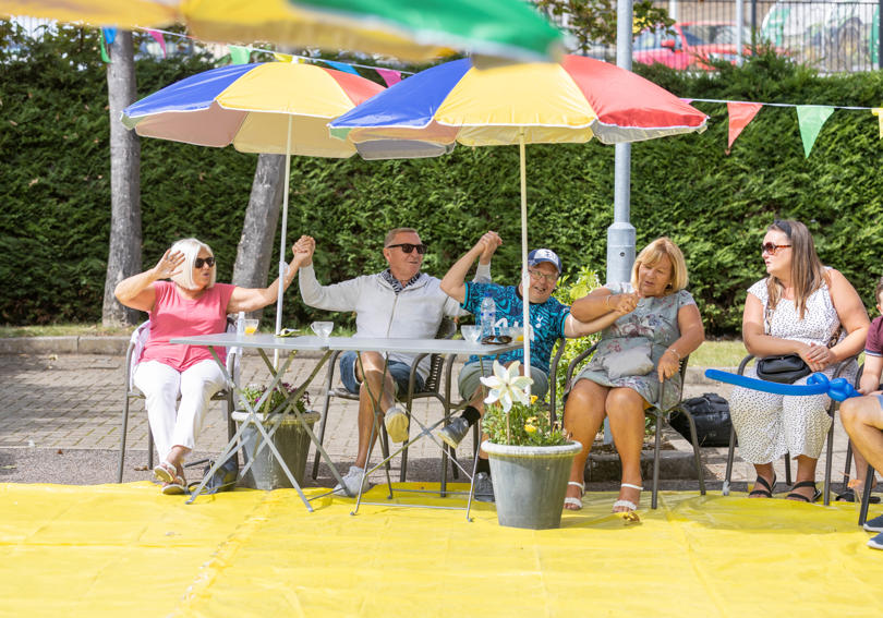 A family sitting outside in the summer under sun umbrellas, looking happy
