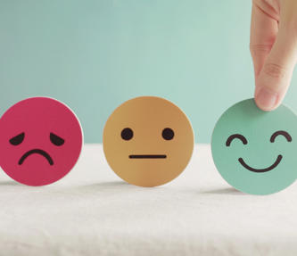 A picture showing a sad, indifferent and happy face. The hand is picking up and choosing the happy face to symbolise their choice to feel happy.