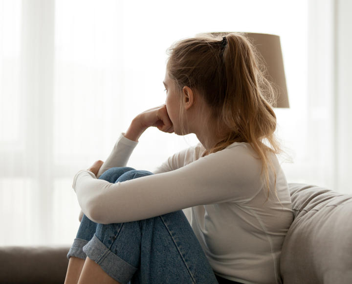 A young woman sits looking towards a window, she seems worried.
