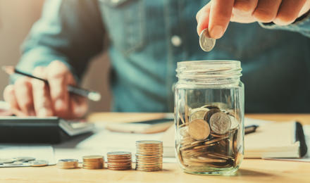 A man is counting money and storing it in a savings jar