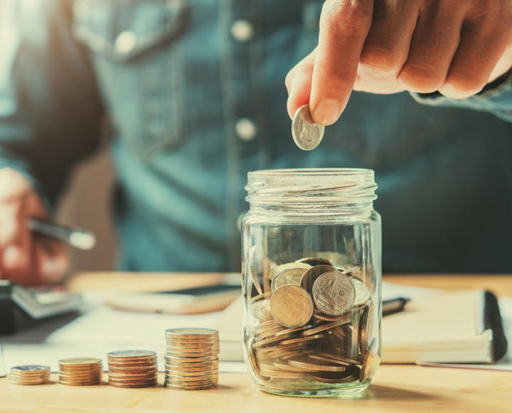 A man is counting money and storing it in a savings jar