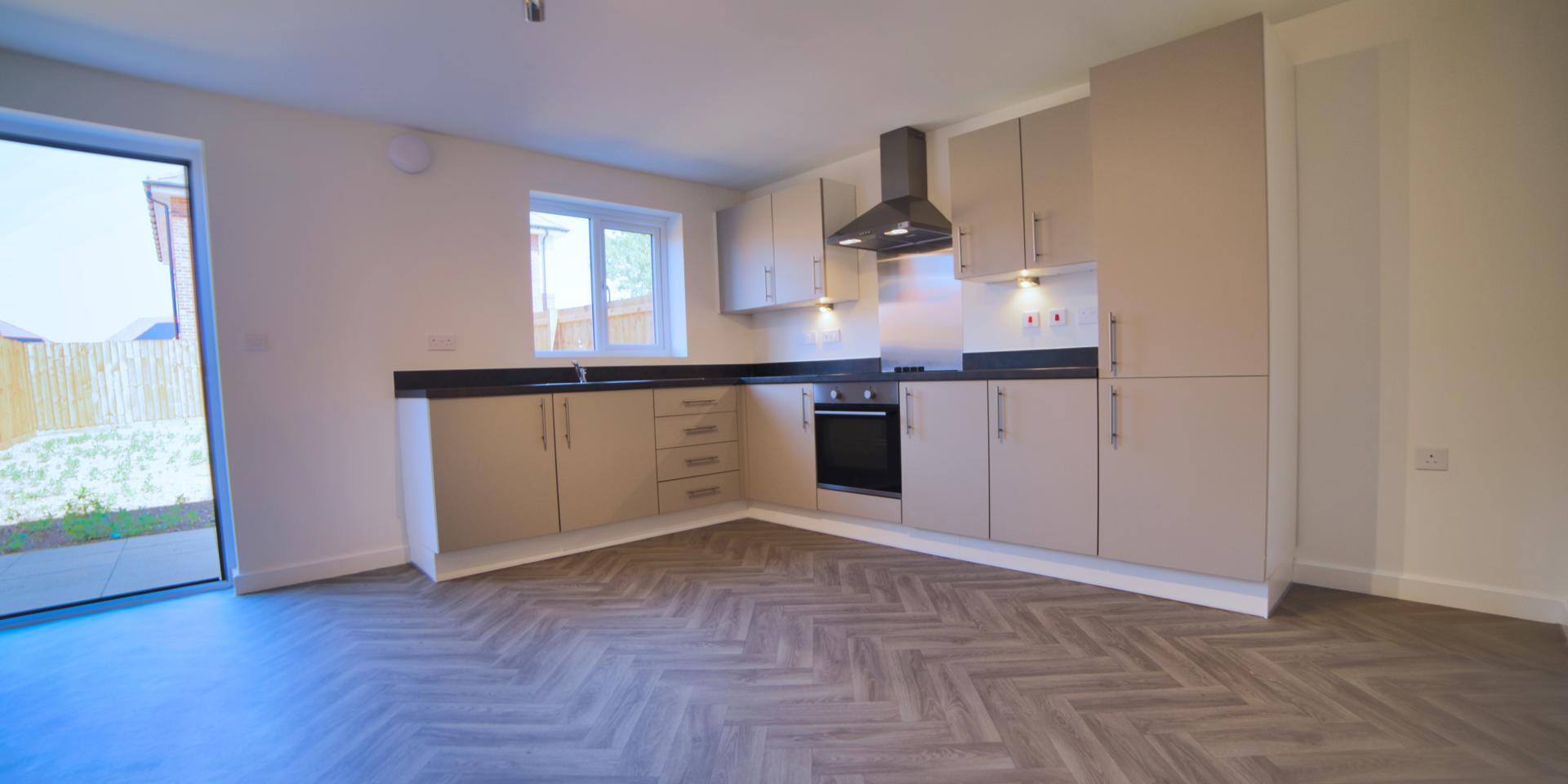 There is an open plan kitchen diner with herringbone effect vinyl flooring