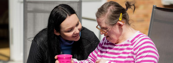 A support worker sitting outside in the sun with a service user, talking and smiling.