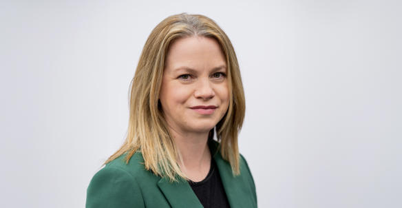 Headshot of Natalie Sturrock, Director of Housing. She is wearing a black top and emerald green blazer and has shoulder length blonde hair and green eyes.