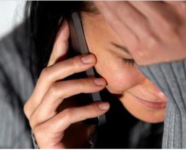A woman speaking on her mobile phone. She is distressed with her hand on her forehead.