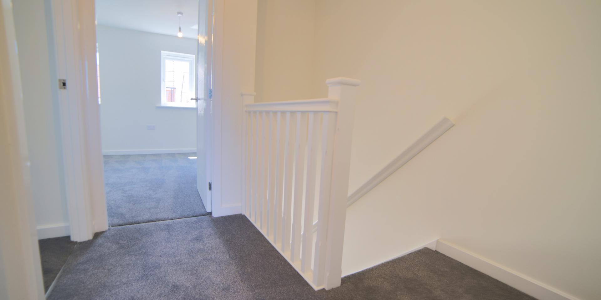 The landing has a white banister and handrail, and grey carpet