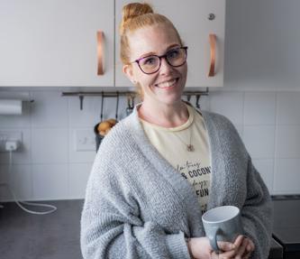Young woman smiling holding a mug of tea in her kitchen