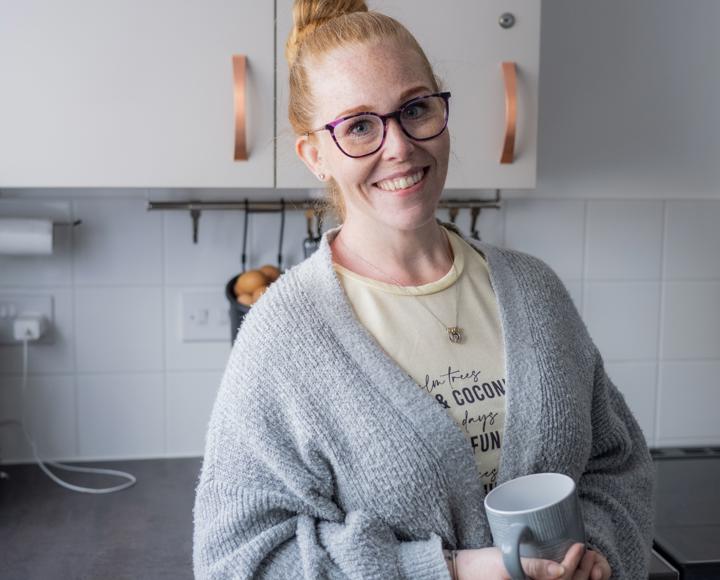 Young woman smiling holding a mug of tea in her kitchen