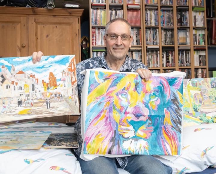 Hightown service user shows his colourful painting of a lion, amongst other paintings