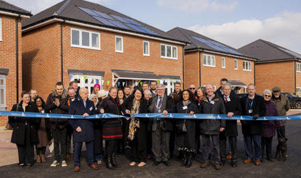 Group of people standing in front of houses and behind a Hightown branded ribbon being cut by Victoria Collins MP