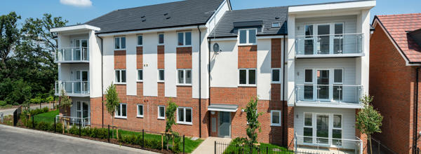 A new block of flats taken on a sunny day. Light brick work and some of it is painted white. Some have glass balconies. 