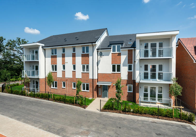 A new block of flats taken on a sunny day. Light brick work and some of it is painted white. Some have glass balconies. 