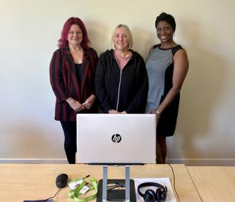 Thre women in the Repairs team smiling standing behind a laptop