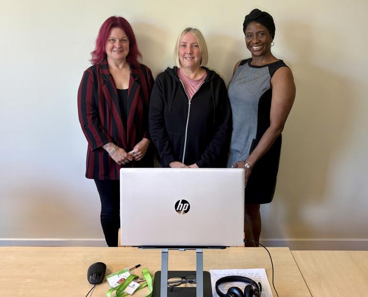 Thre women in the Repairs team smiling standing behind a laptop