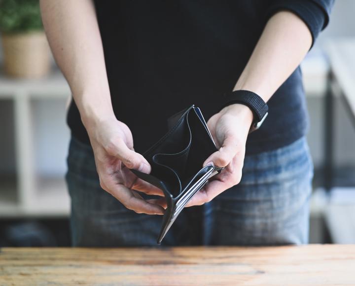 A man standing up, holding out his wallet which is empty. You cannot see the mans head