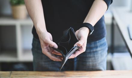 A man standing up, holding out his wallet which is empty. You cannot see the mans head