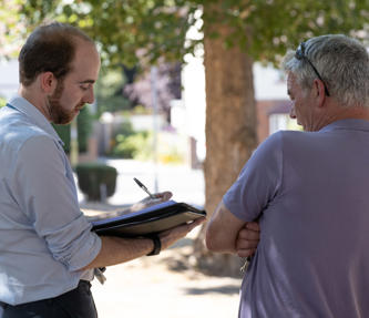 A member of staff is stood outside taking notes whilst talking to a resident