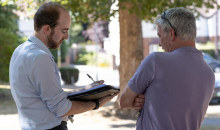 A member of staff is stood outside taking notes whilst talking to a resident